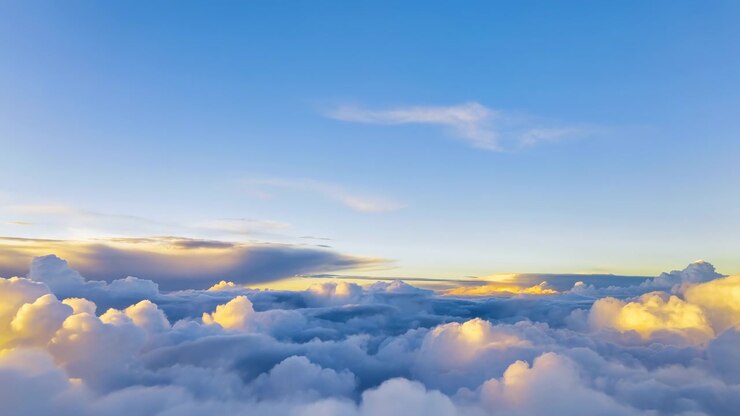 Vaste paysage nuageux de haute altitude montrant des couches denses de cumulus et de stratocumulus remplissant la vue inférieure, tandis qu'un ciel bleu clair avec de fines volutes de cirrus s'étend au-dessus, brillant d'une douce lumière dorée.