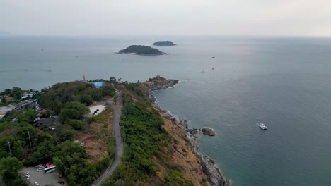 drone view of promthep cape, phuket, thailand, showing rugged coastline, lush greenery, and boats in tropical waters.