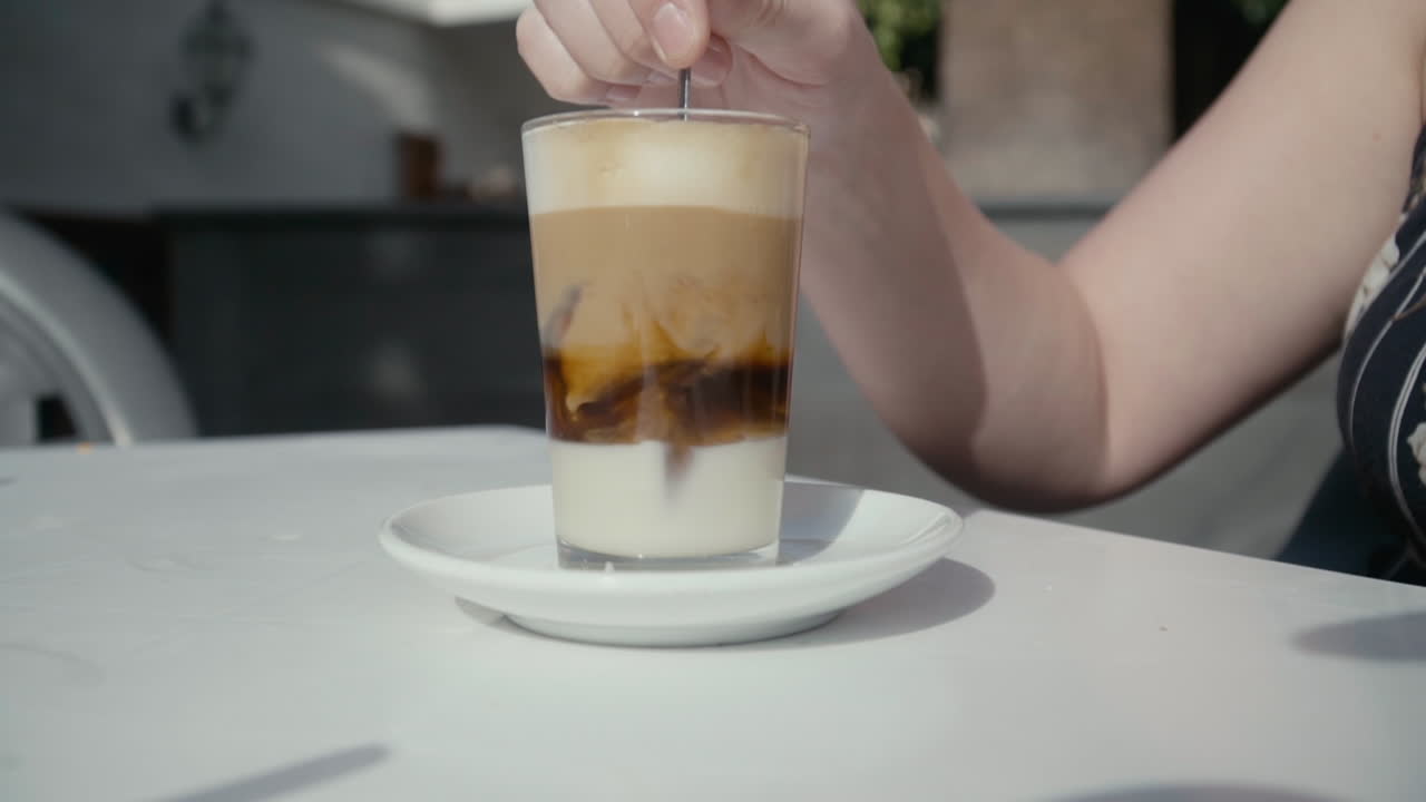 여자는 티스푼을 사용하여 유리에 있는 바라키토 음료를 휘젓고, 닫고, 느린 동작
