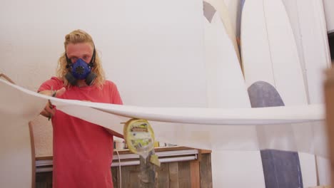 fabricante de tablas de surf masculino caucásico con una máscara facial y haciendo una tabla de surf