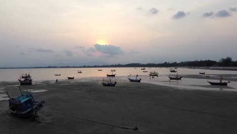 Drone-footage-of-boats-beached-on-the-coast-during-low-tide-at-Khao-Ta-Mong-Lai-Bay,-Thailand-during-sunset