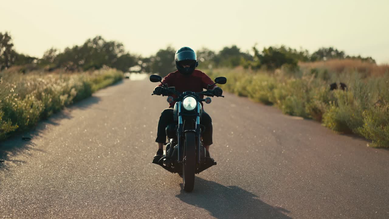 мотоциклист в красной куртке и в шлеме едет по дороге в солнечное время с ветром