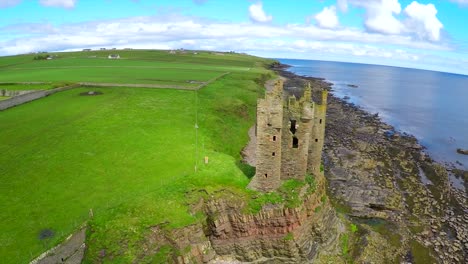 a beautiful aerial shot over an abandoned castle along the north coast of scotland