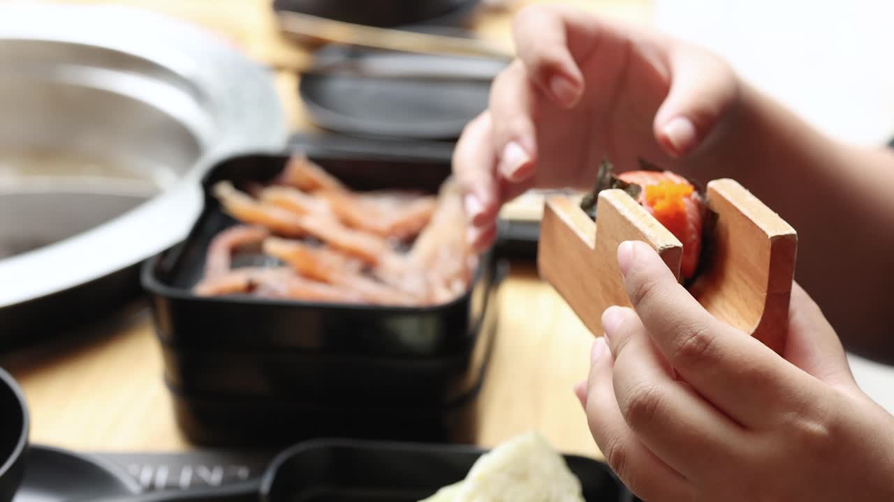 Person selects assorted sushi nigiri with chopsticks in bright dining setting, close-up perspective