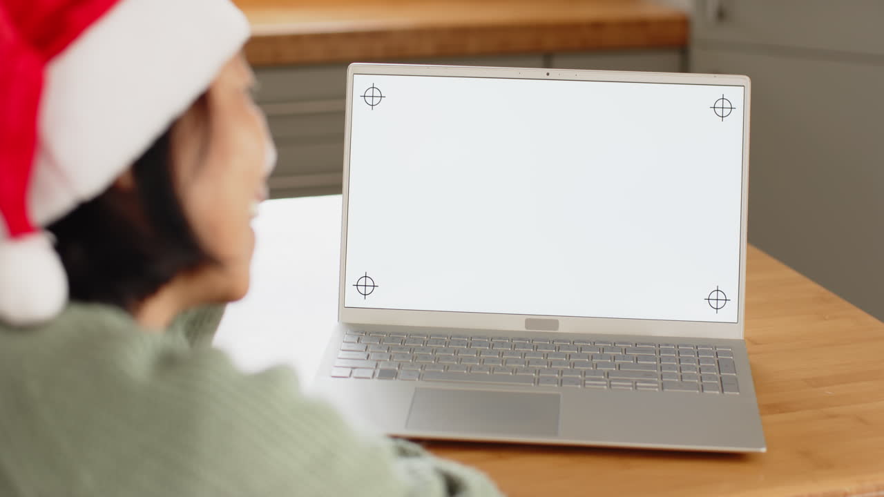 Senior wearing Santa hat video chatting on laptop at home during Christmas, copy space