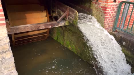 Slow-motion-close-up-of-splashing-water-flowing-down-beside-vintage-waterwheel-outdoors-in-nature