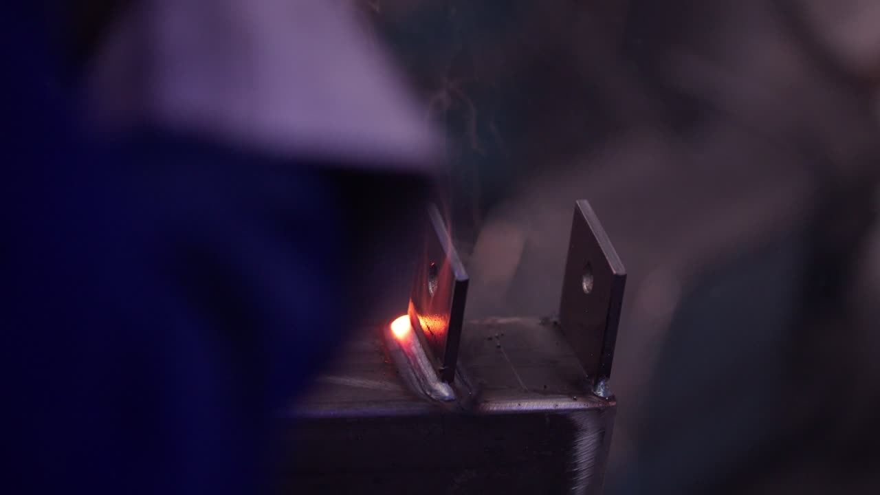 Close-up of a person melting iron hinges to a bar, sparks flying in the process