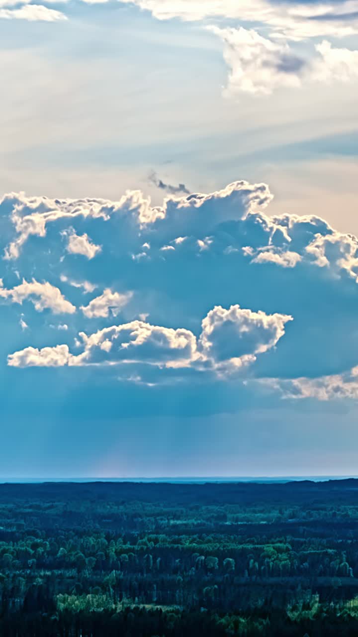 Timelapse aereo di nuvole stratificate che si muovono nel cielo sopra un vasto paesaggio boscoso, con sottili cambiamenti di luce che creano un'atmosfera calma e suggestiva, verticale.