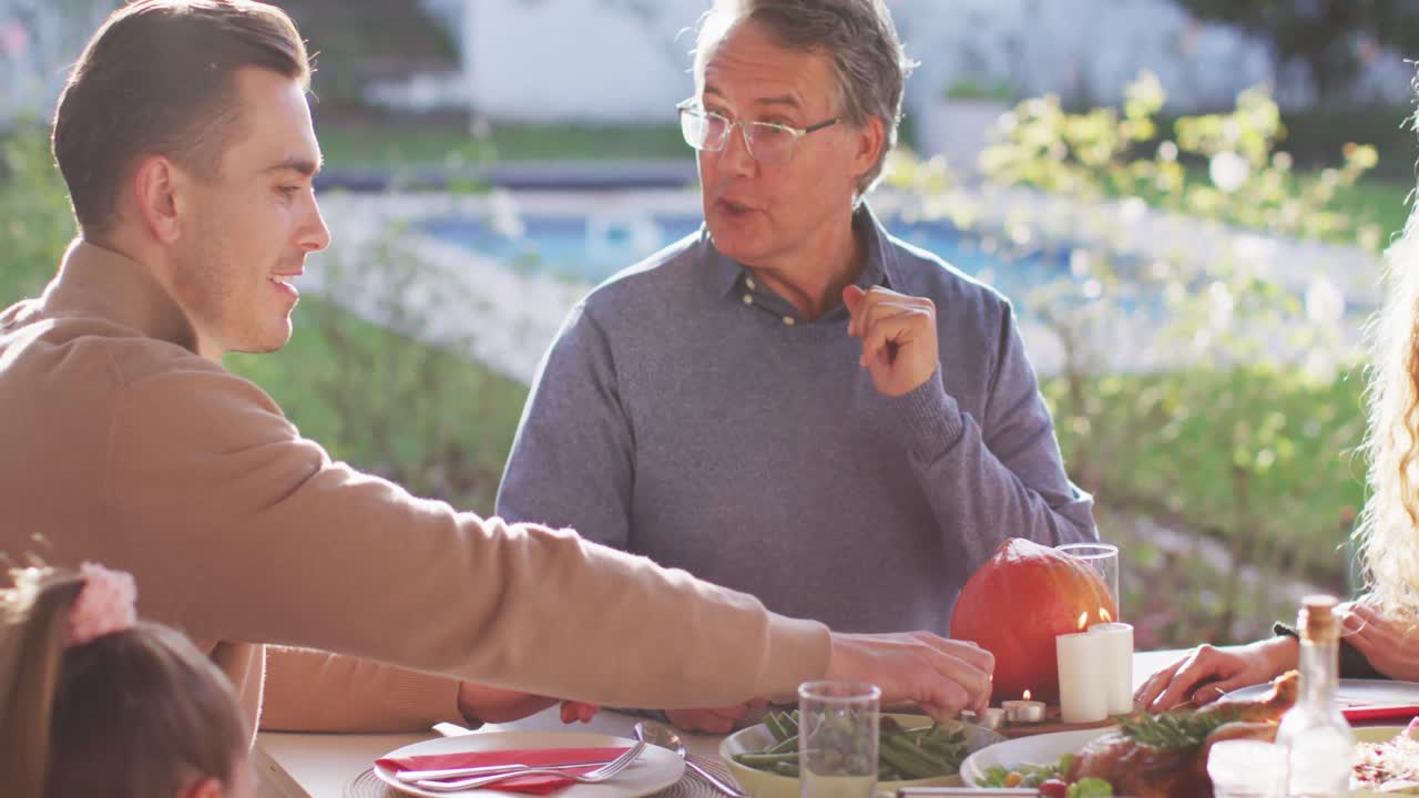 행복한 백인 부모, 딸, 할아버지가 야외 테이블에 앉아 가족 식사를 하는 동영상