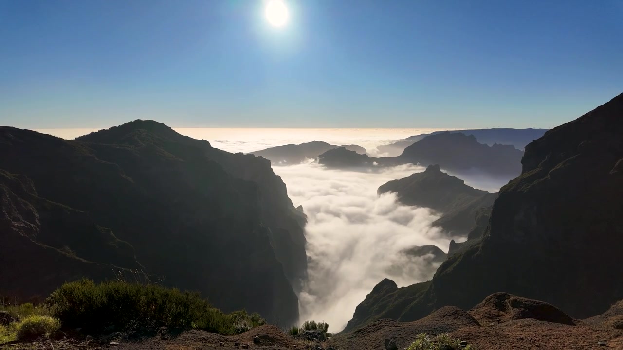 Plan fixe capturant les sommets du Pico do Arieiro s'élevant au-dessus d'une mer de nuages sous un soleil de midi éclatant sur l'île de Madère, Portugal.