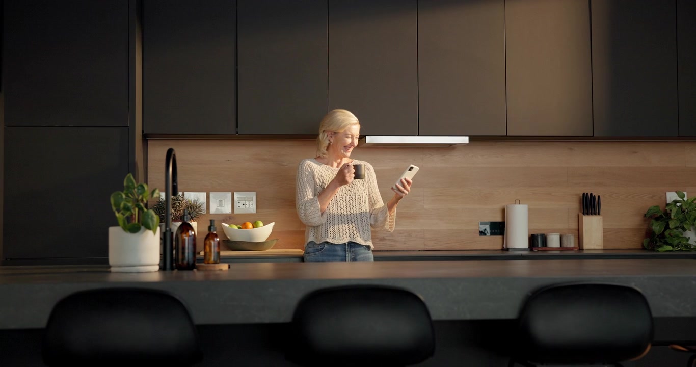 Donna che beve caffè e usa lo smartphone in una cucina moderna