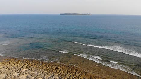 無人機輕輕地降落,望向遙遠的島<unk>,前景有珊瑚礁和青<unk>色海面,以及獨特的珊瑚礁與珊瑚礁