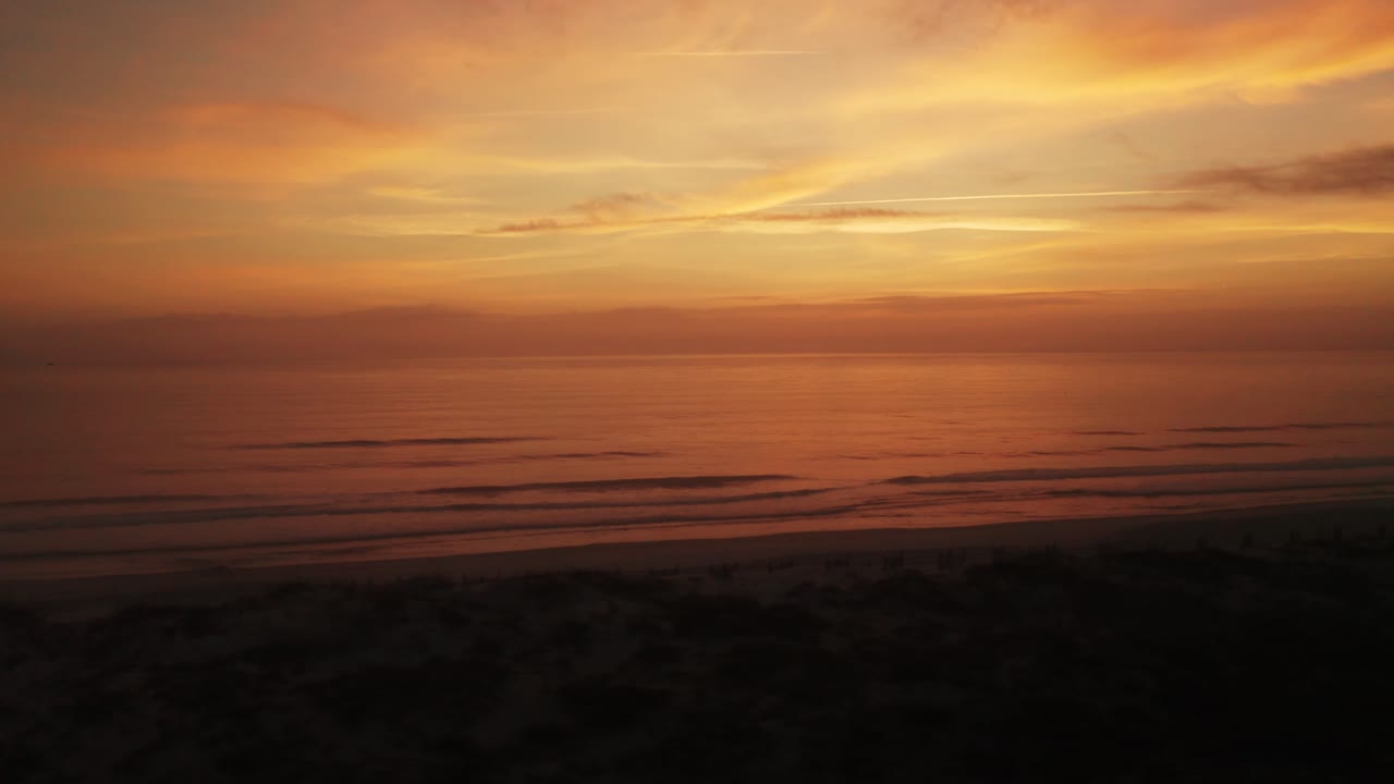 vista aérea sobre una playa al atardecer con un pájaro volando a través del horizonte lejano