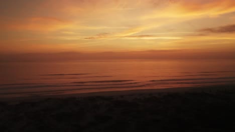 aerial view over a beach at sunset with a bird flying across the distant horizon