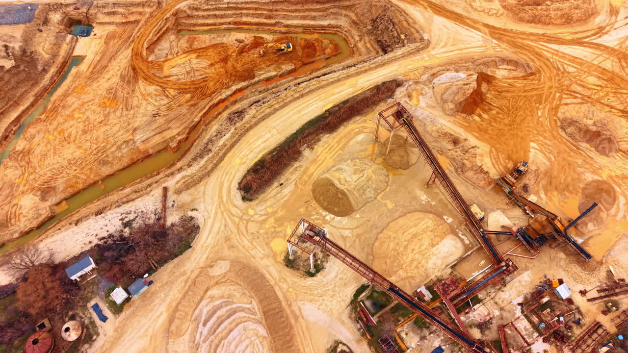 High angle view of industrial sand quarry and conveyor structures. Wide aerial shot of open pit mine featuring sand piles, processing equipment and heavy machinery