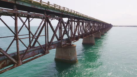 old rusted metal support beams hold up bridge and piping across ocean on concrete stilt supports