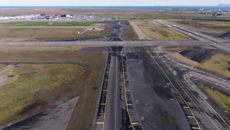 Straight-taxiway-tarmac-on-open-empty-airfield-in-Iceland,-drone-shot