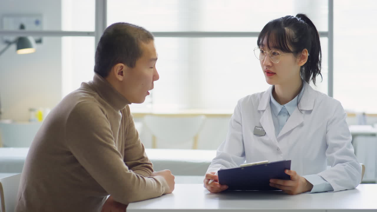 Asian Female Doctor Giving Consultation to Man in Medical Office