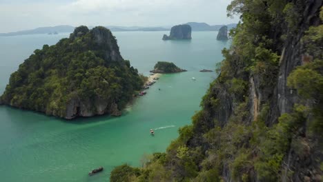 Aerial-shot-passing-next-to-a-limestone-island-revealing-other-islands,-beaches-and-long-tail-boats-in-the-Andaman-sea