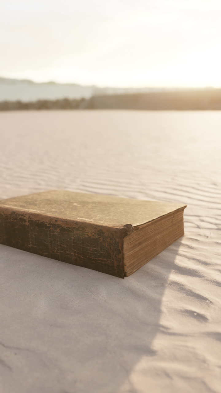 A Vintage Book Lies Alone on a Sandy Beach at Sunset