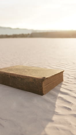 a vintage book lies alone on a sandy beach at sunset