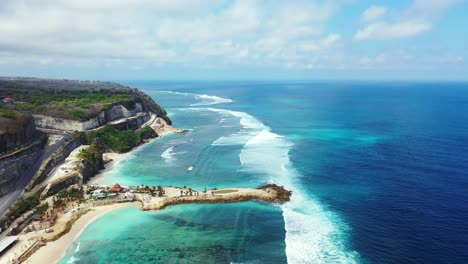 Big-waves-of-blue-ocean-splashing-on-calm-turquoise-lagoon-with-corals-and-cliffs-near-rocky-shore-of-tropical-island-in-Indonesia