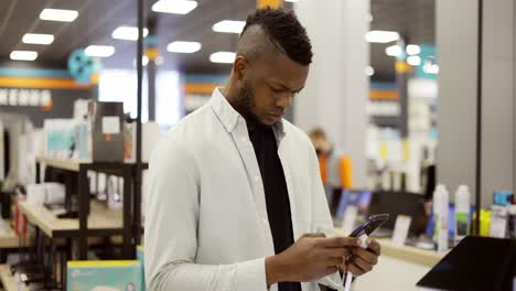 concentrated man in mask is choosing a new mobile phone in a shot, checking how it works