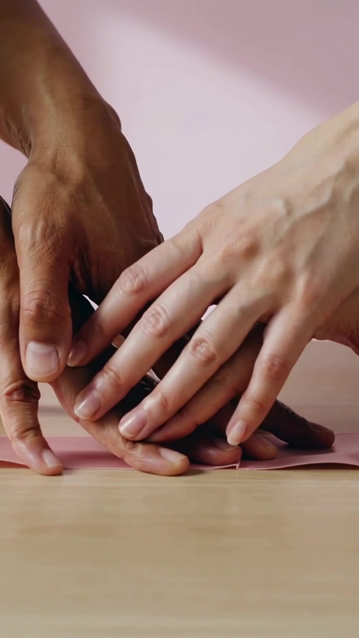 Vertical video: Right hand entering, two hands picking stone on pink sheet at table for shared grip