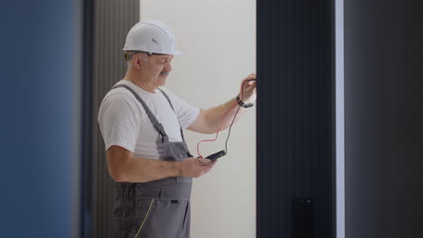 elderly in a helmet electrician checks the operation of the wall control unit of lamps with the system of a modern house after installation and repair