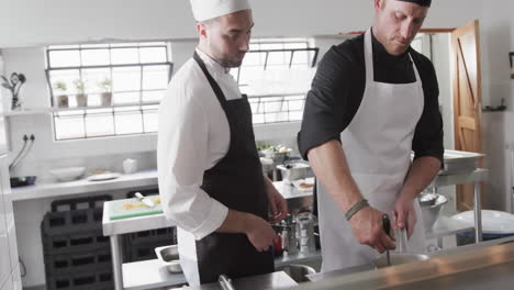 focused caucasian male chef instructing trainee male chef in kitchen, slow motion