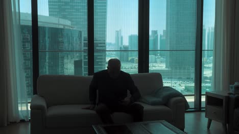 silhouette of a man in an urban apartment siting down to read email or social media from a smartphone