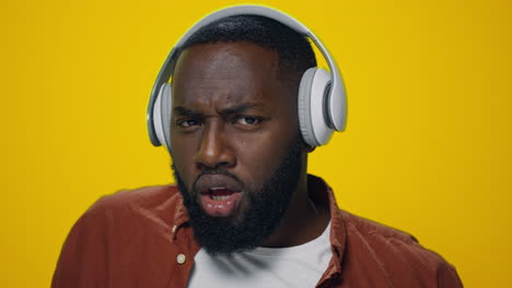 portrait of happy african man dancing in headphones on yellow background.