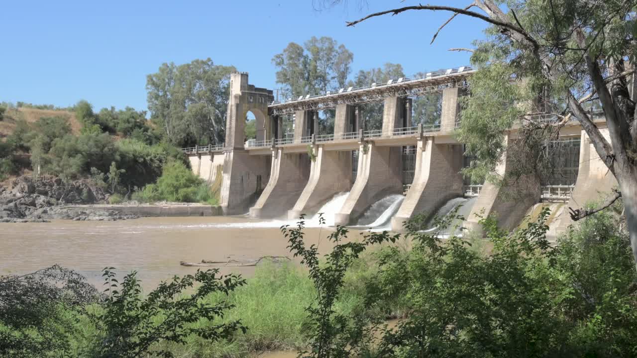 General view of an architectural construction of a dam on the Guadalquivir river with the sluice gates open on a sunny day