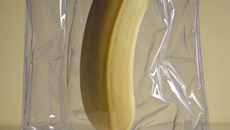 single ripe banana is encased in a shiny, transparent plastic wrap, showcasing its smooth texture and vibrant color. the minimalist background emphasizes the fruit's natural appeal