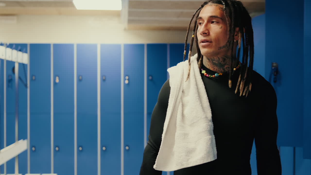 Uomo con dreadlock e tatuaggi in piedi in uno spogliatoio
