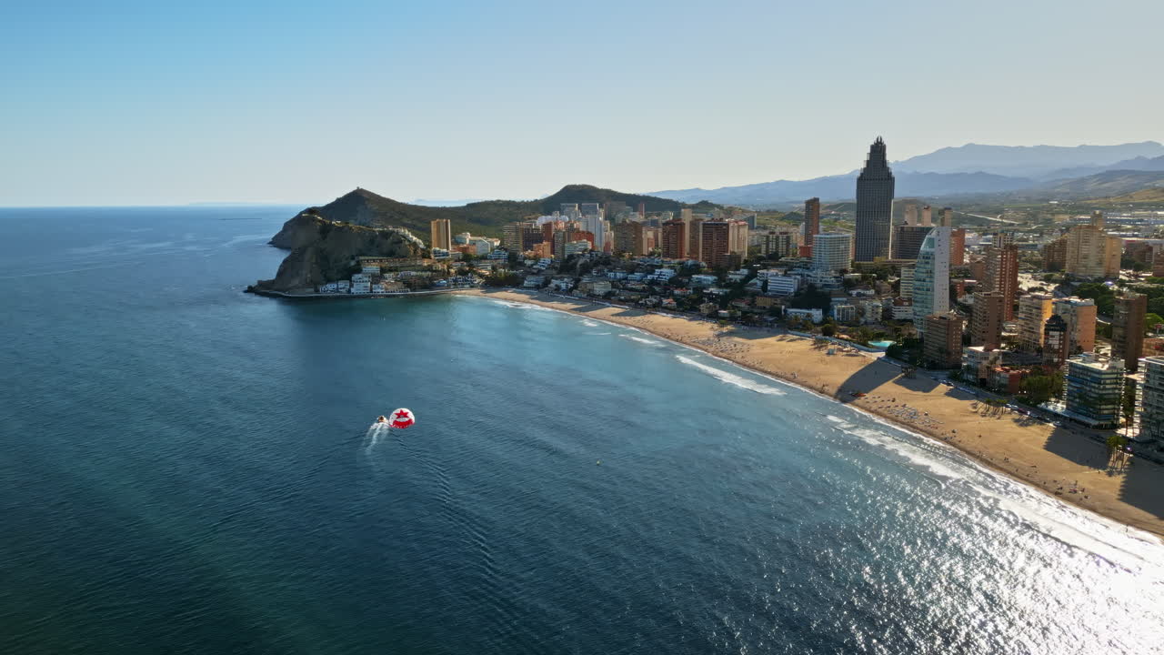 Vista aerea da drone degli edifici lungo la costa con persone che fanno parapendio sul mare a Benidorm, in Spagna, alla luce del giorno