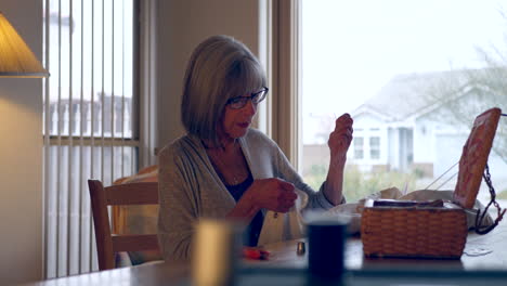 A-pretty-middle-aged-woman-sewing-a-button-onto-a-white-dress-shirt-by-hand-with-a-needle-and-thread