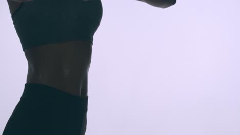 mujer delgada y en forma estirándose con gotas de sudor formándose en su torso musculoso - fondo brillante