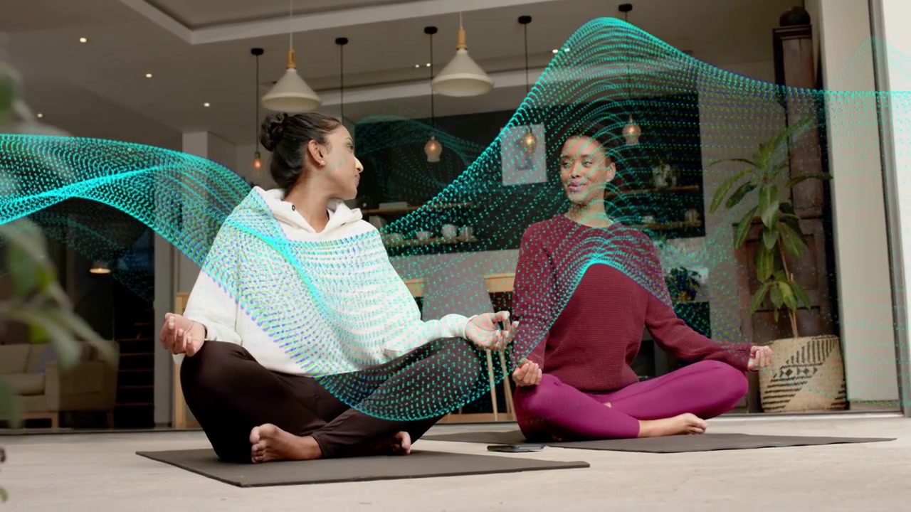 Duas mulheres meditando em tapetes de yoga, abrindo os olhos enquanto uma onda pontilhada turquesa varre, causando um sorriso