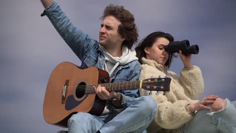 a young boy plays the guitar and a young girl looks around with a pair of binoculars on the roof of a caravan.