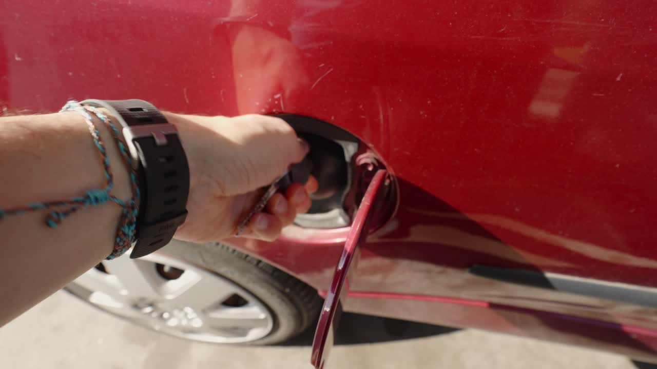 punto de vista de una persona que cierra una tapa del tanque de combustible con una llave de un coche rojo
