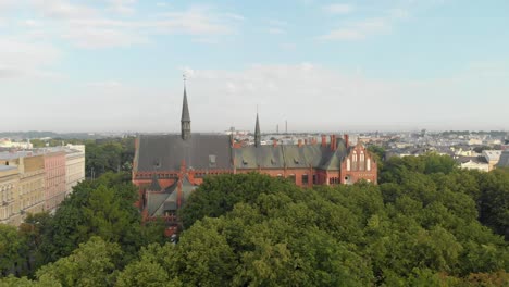 Scenic-aerial-shot-of-Art-Academy-of-Latvia-on-sunny-day,-drone-rising-above-trees