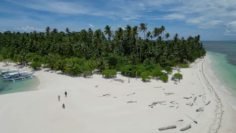 Tourists-roam-on-white-sandy-beach-with-driftwood-and-banca-outrigger-canoes,-aerial-pullback