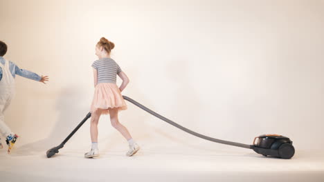 little boy is running away from the girl with a vacuum cleaner in her hands. funny kids are playing while cleaning