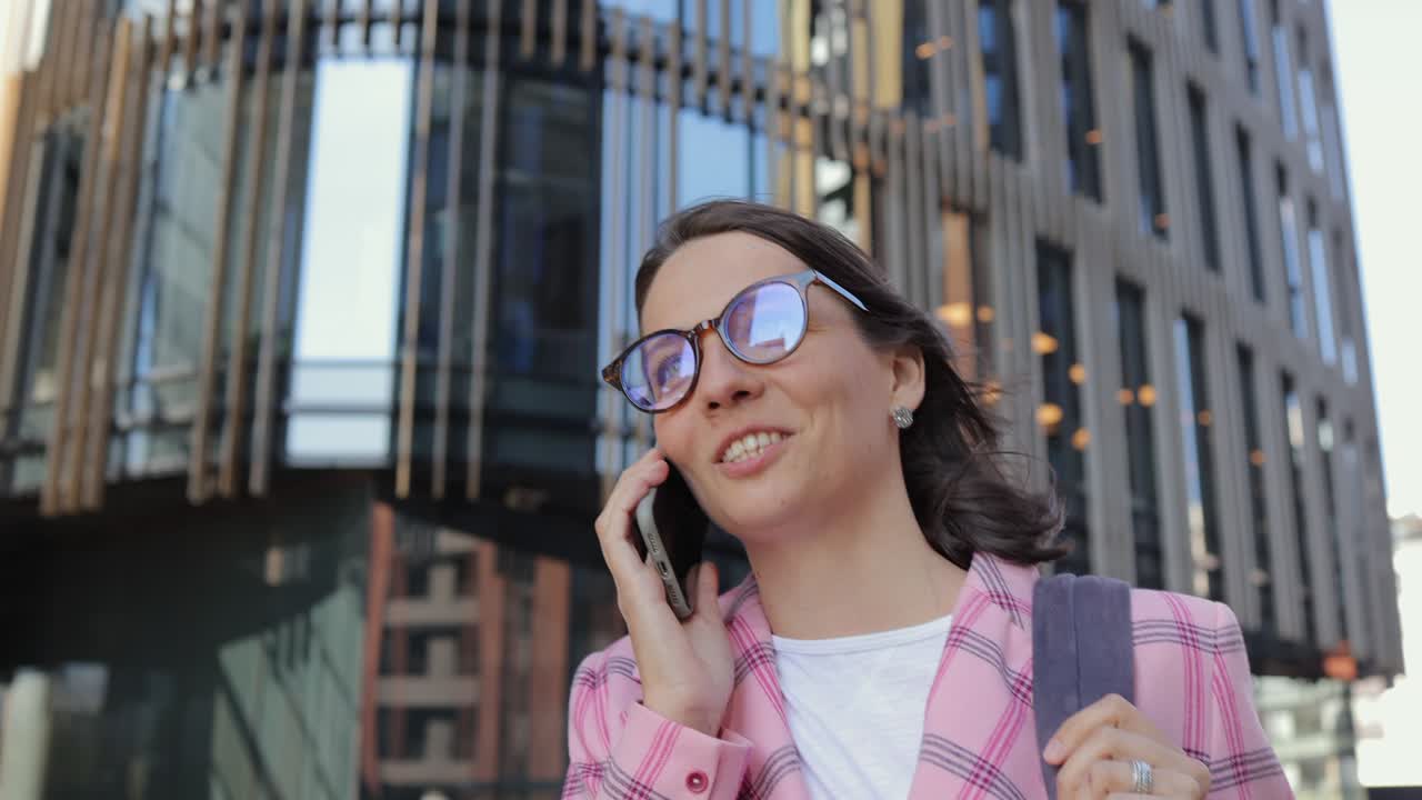 woman with glasses is walking down the street and talking on the phone. a confident business woman goes to work in the office and talks on a smartphone