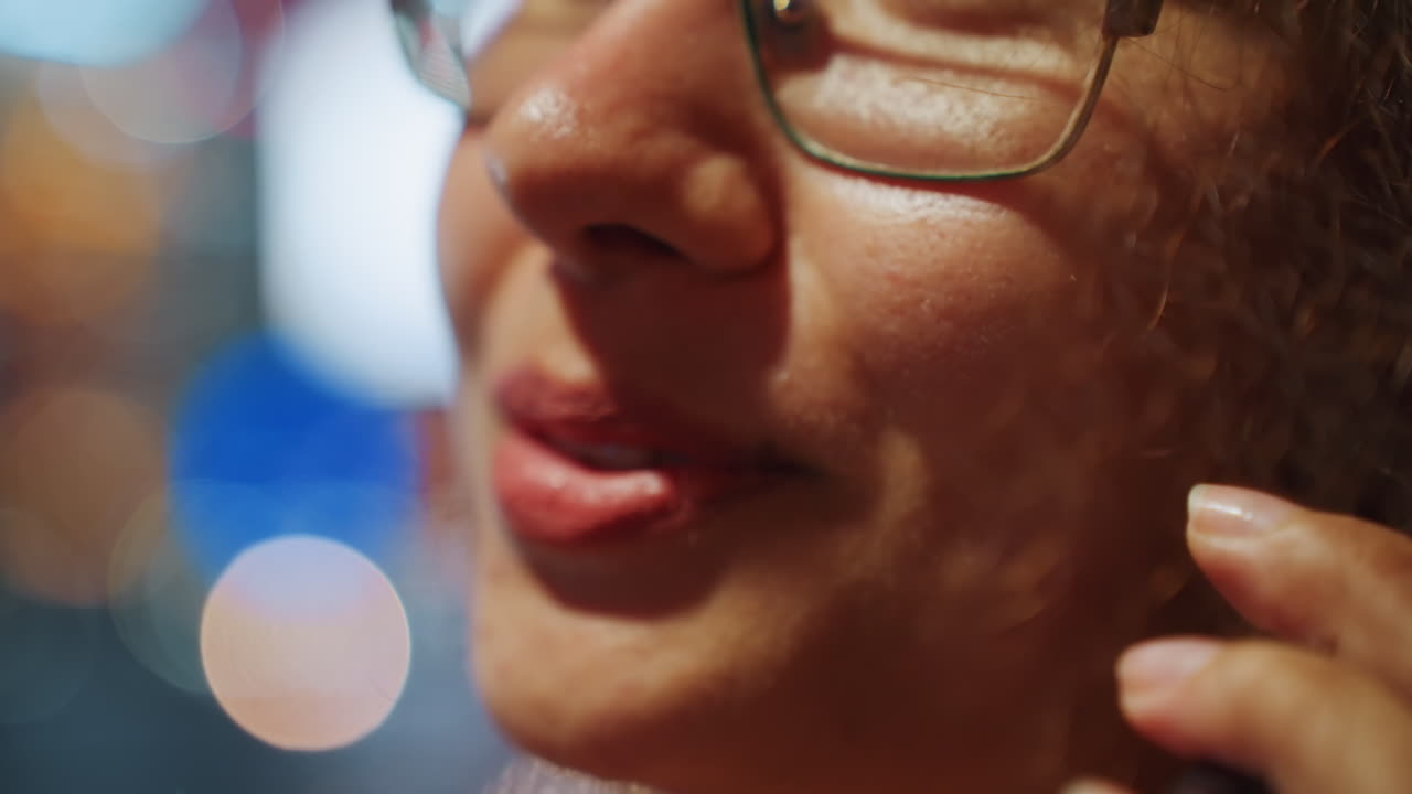 Neon bokeh fonuyla telefona konuşan dudakların yakın çekimi, samimi kentsel gece mesajı, hafif gülümseme ve ağız hareketleri, gözlük çerçevesi görünür, yumuşak sıcak cilt dokusu, samimi ses anı.