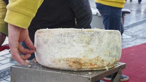 Man cutting a large wheel of cheese at a market
