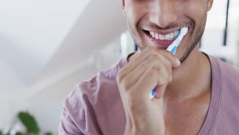 Close-up-of-happy-biracial-man-brushing-teeth-in-sunny-bathroom-in-the-morning,-slow-motion