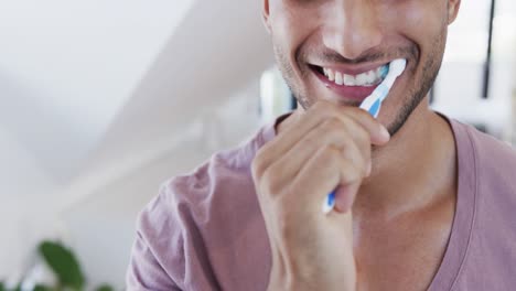 Primer-Plano-De-Un-Hombre-Birracial-Feliz-Cepillándose-Los-Dientes-En-Un-Baño-Soleado-Por-La-Mañana,-Cámara-Lenta