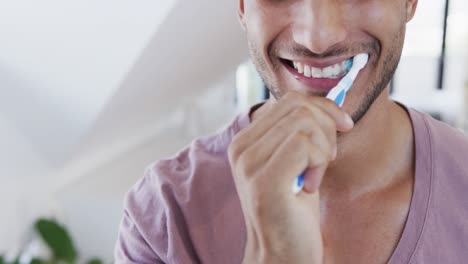 primer plano de un feliz hombre biracial cepillándose los dientes en un baño soleado por la mañana, cámara lenta